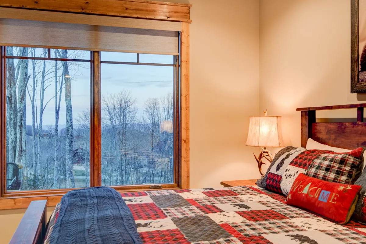 A cozy bedroom with plaid bedding and a large window that looks out onto the trees, inviting guests to unwind while soaking in the peaceful scenery. Soft lighting and decorative touches create an intimate, romantic atmosphere.