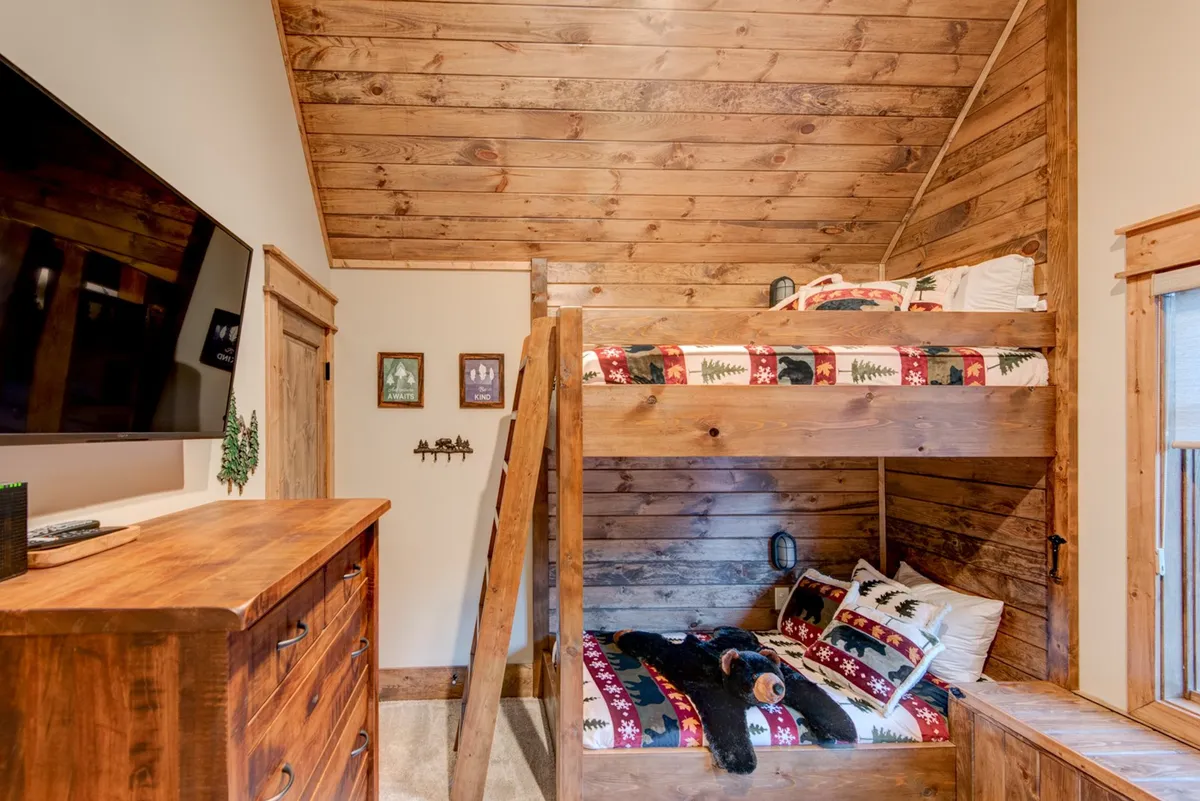 A cheerful bunk room with sturdy wooden bunk beds, a dresser, television, and playful decor. The room is designed for younger guests or siblings, providing a fun and functional sleeping area for families or groups with children.