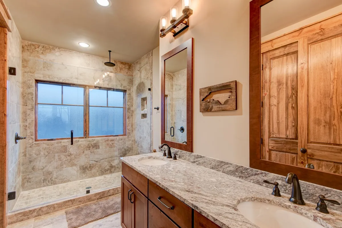 A modern bathroom featuring double vanity sinks, a large shower area with glass doors, and ample natural light streaming through windows. The finishes are clean and spa-inspired, offering a serene space for relaxation and daily routines.