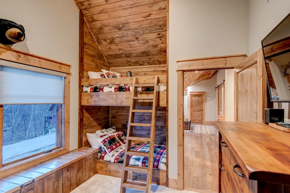 A cheerful bunk room with two sets of built-in twin-over-twin beds, a wooden ladder, a window seat, and a dresser. The space is designed for fun and comfort, perfect for children or friends to share sleepovers and create memories.
