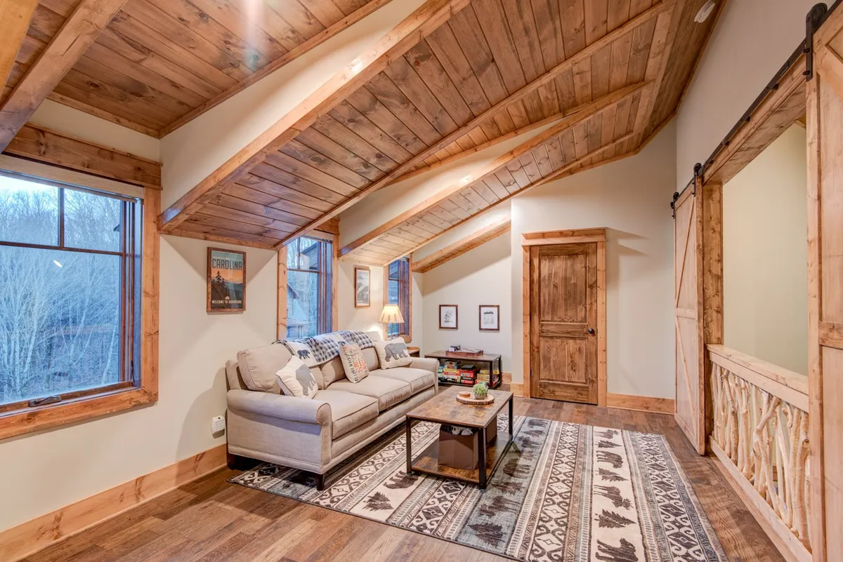 A warm, welcoming living area with a sofa, rug, exposed wooden beams, and large windows. The coffee table provides a central spot for board games or casual gatherings, and the natural light creates an airy, cheerful ambiance ideal for play and relaxation.