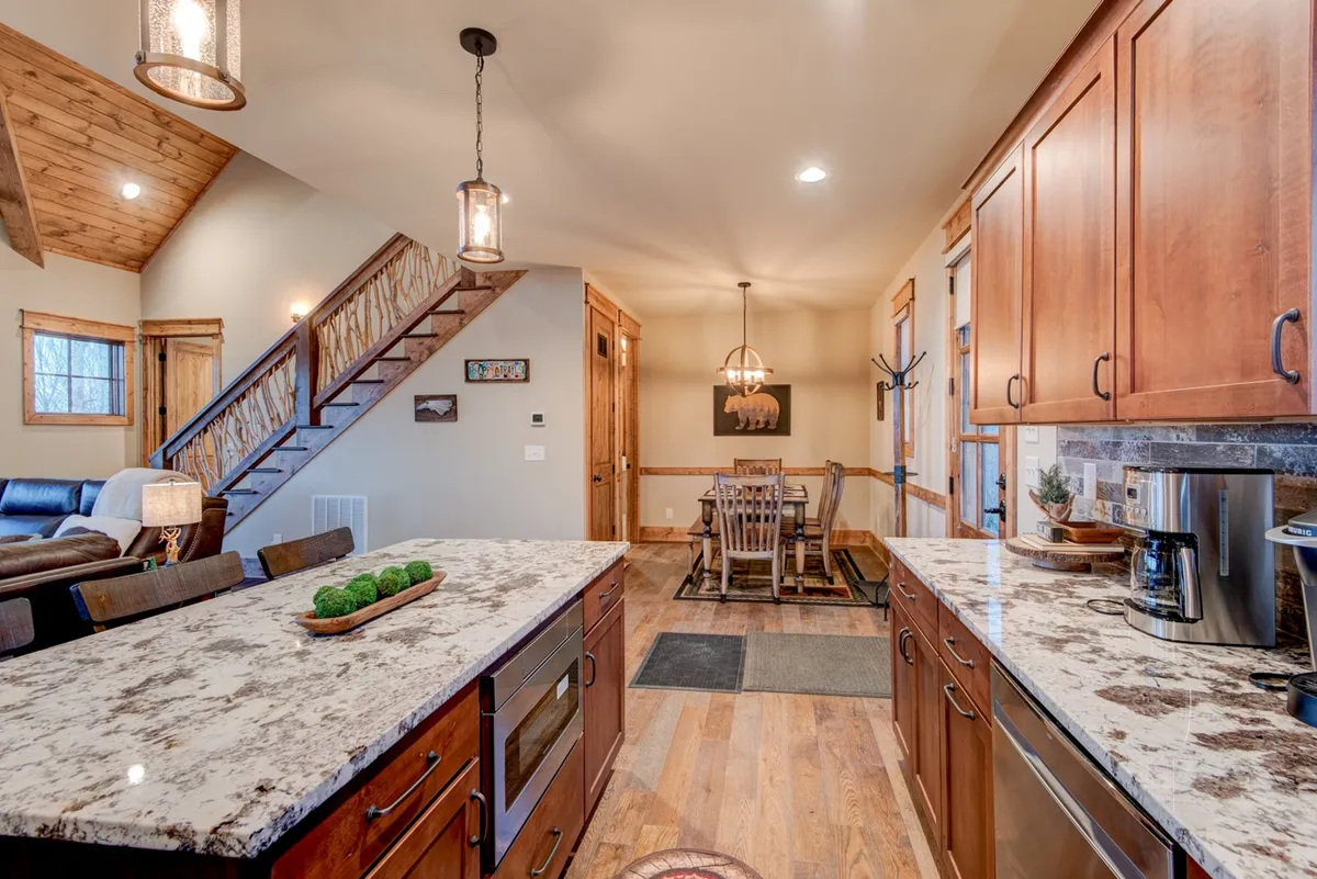 An open-plan kitchen and dining area featuring a central kitchen island with granite countertops, a six-seat dining table, and stylish lighting. The layout allows for seamless transitions between cooking, dining, and socializing.
