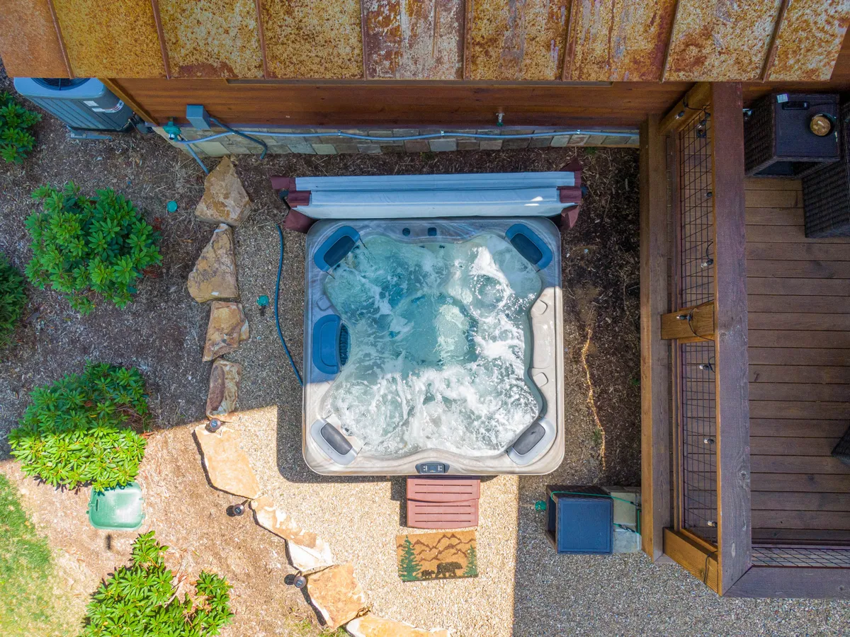 A serene patio with a bubbling hot tub nestled among greenery. The area feels private and inviting, ideal for late-night relaxation or taking in the fresh mountain air after a day of adventure.