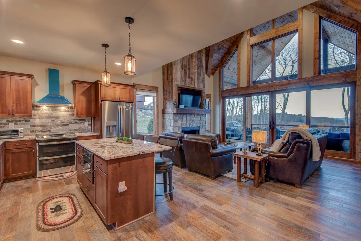A bright, open concept kitchen and seating area featuring a large island, inviting fireplace, and expansive windows. The setup encourages communal cooking, informal dining, and cozy family time, accommodating groups of all sizes.