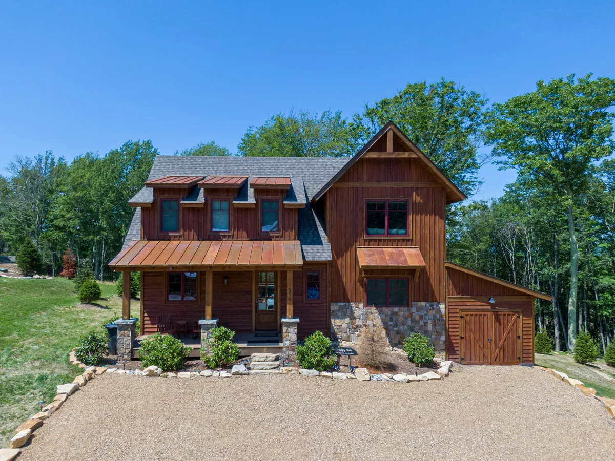 This image captures the home's wooden facade with stone accents, a welcoming front porch, and landscaped garden. The porch area hints at a pet-friendly entrance and a great spot to start outdoor adventures or return to after exploring the nearby trails.