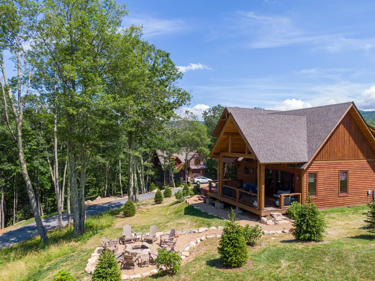 A welcoming exterior shot featuring a wooden cabin surrounded by trees, with a patio, fire pit, and comfortable seating. The scene suggests possibilities for family barbecues, stargazing, and easy access to nearby trails, with the fire pit as a focal point for post-adventure relaxation.